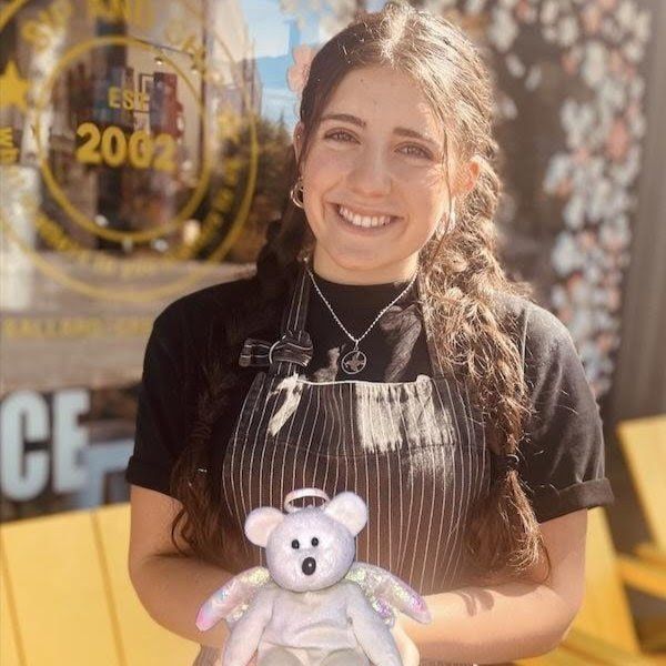 Smiling person holding a small plush bear in front of a store window