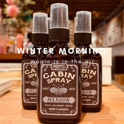 Three cabin spray bottles on a wooden counter, labeled “Winter Morning” and “Magic in the Air”