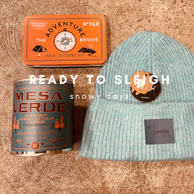 Orange tin, black mug, and blue knit beanie arranged on a beige surface.