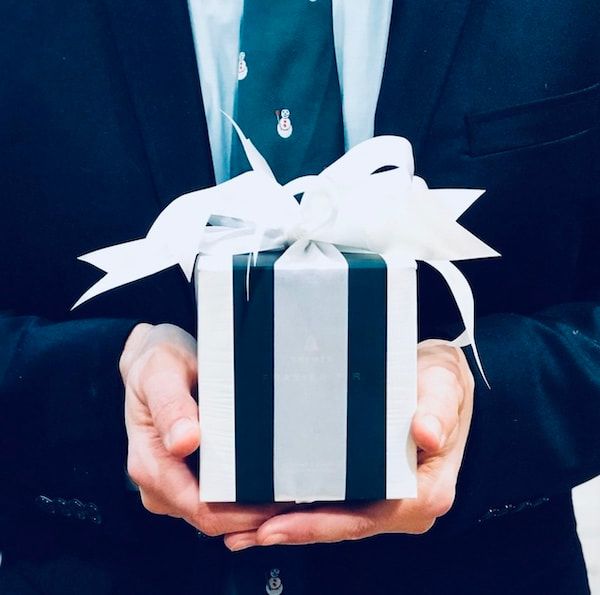 Hands holding a white gift box with a ribbon on a dark background