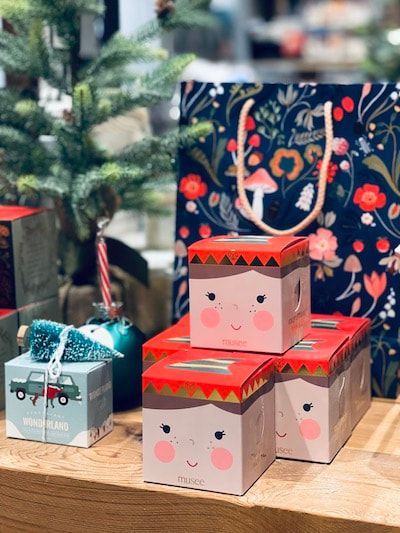 Decorative gift boxes with faces, stacked on a table beside a small wrapped present and a holiday bag.