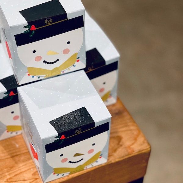 Stacked snowman gift boxes with smiling faces on a wooden table