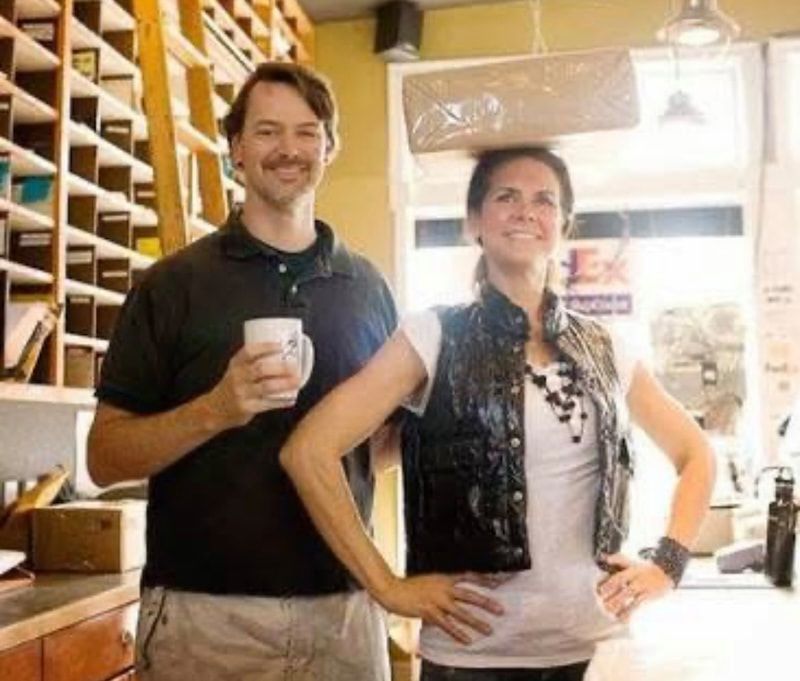 Two people standing in a bright store, smiling and posing near shelves and a counter.