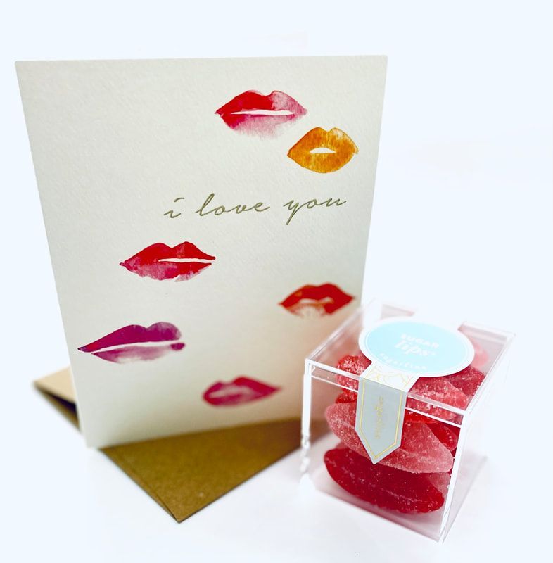 Greeting card with lipstick kiss prints and “i love you,” beside a small clear gift box with a red candle.