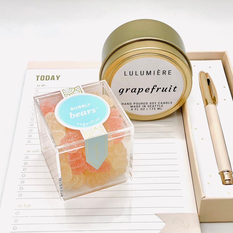 Minimal desk setup with a gold candle, colorful gummy bears box, and pen on a white notepad
