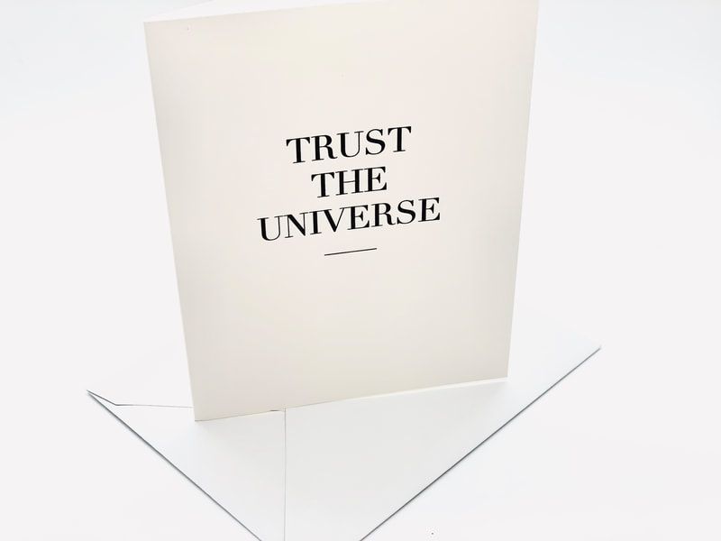 White card with the words “TRUST THE UNIVERSE” above thin angular lines on a pale background