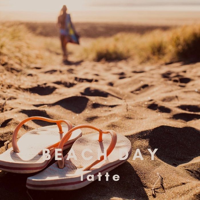 Sandals on a sandy beach with a blurred person in the background; text reads “BEACH DAY” and “liffe”