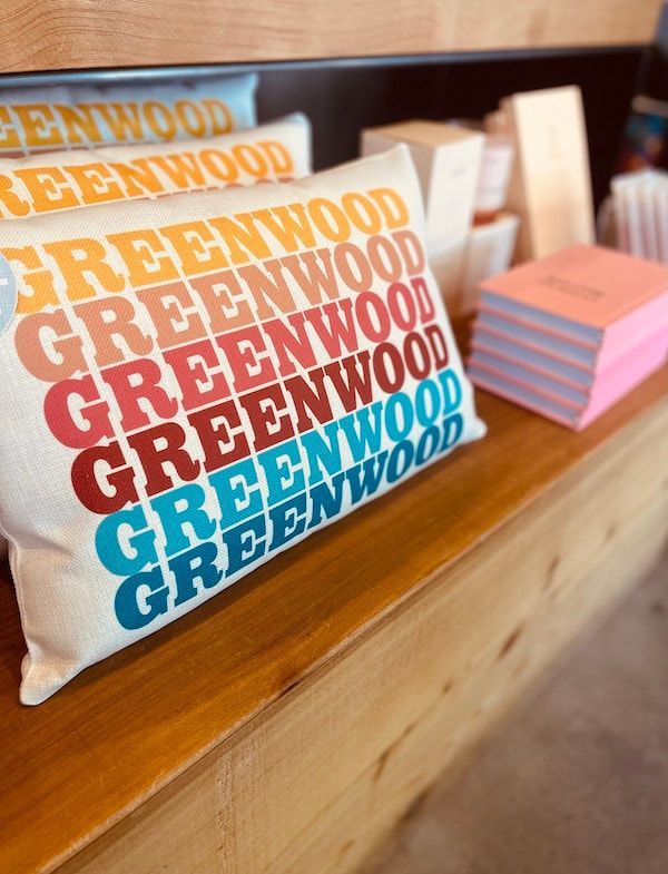 Stacked GREENWOOD logo cards on a wooden counter beside a small pink note stack.