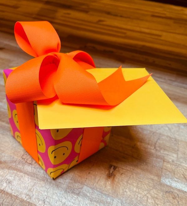 Colorful gift box with orange bow and yellow card on a wooden surface