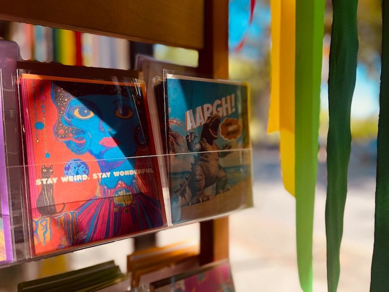 Colorful CDs displayed on a wooden shelf near hanging green ribbons and a sunlit window