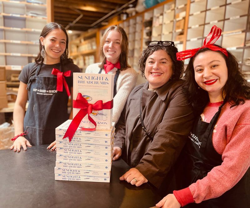 Four smiling staff members holding a gift box with a red ribbon in a shop