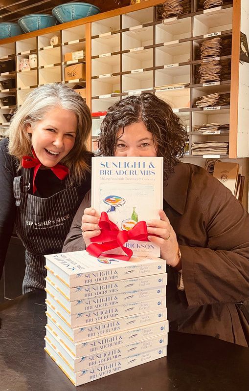 Two people smiling behind a stack of books with a red ribbon in a bookstore-like setting