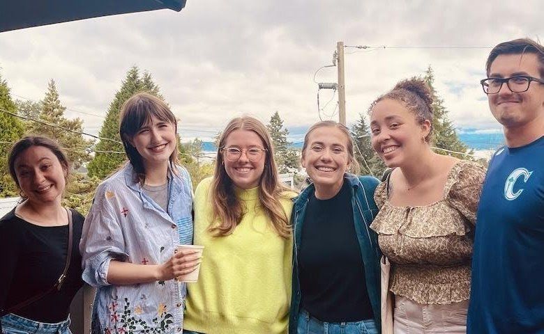 Five smiling friends standing outdoors, posing together in casual clothes at dusk.