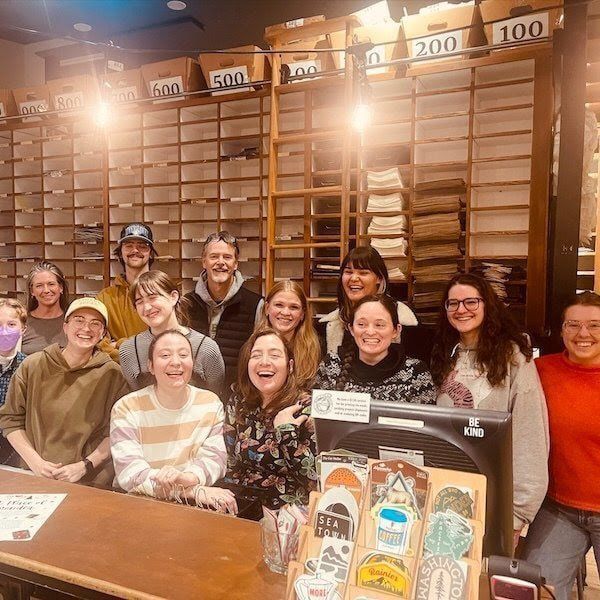 Group of smiling people inside a wooden shoe store with shelves of clogs and a display case in front.