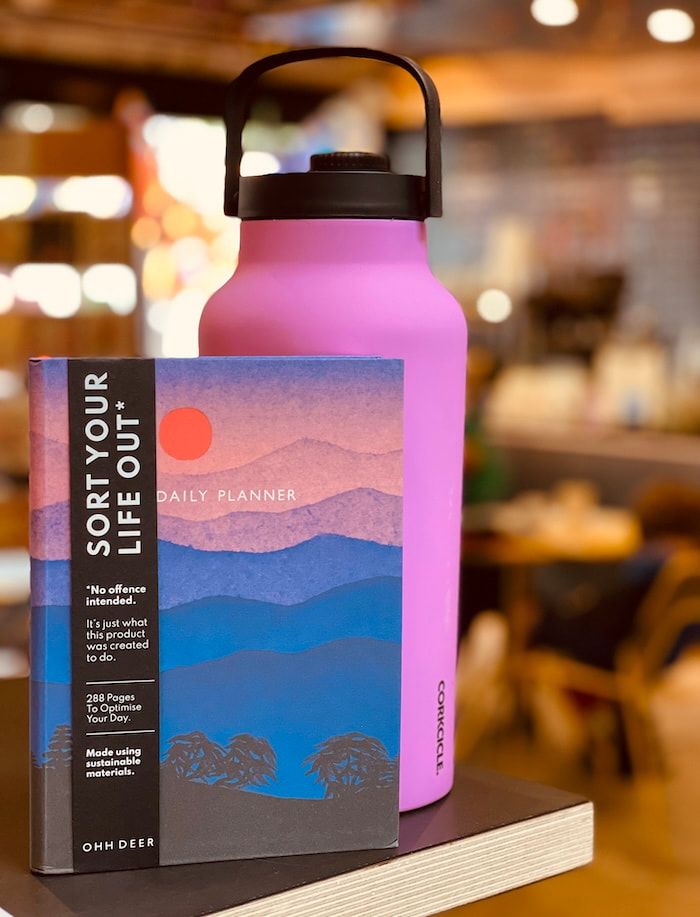 Pink water bottle beside a “Sort Your Life Out” book on a store shelf, with a blurred warm interior background