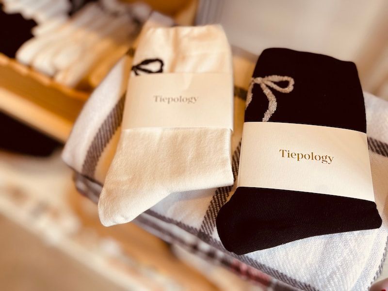 Folded Tieology socks in cream, gray, and black displayed on a shelf.
