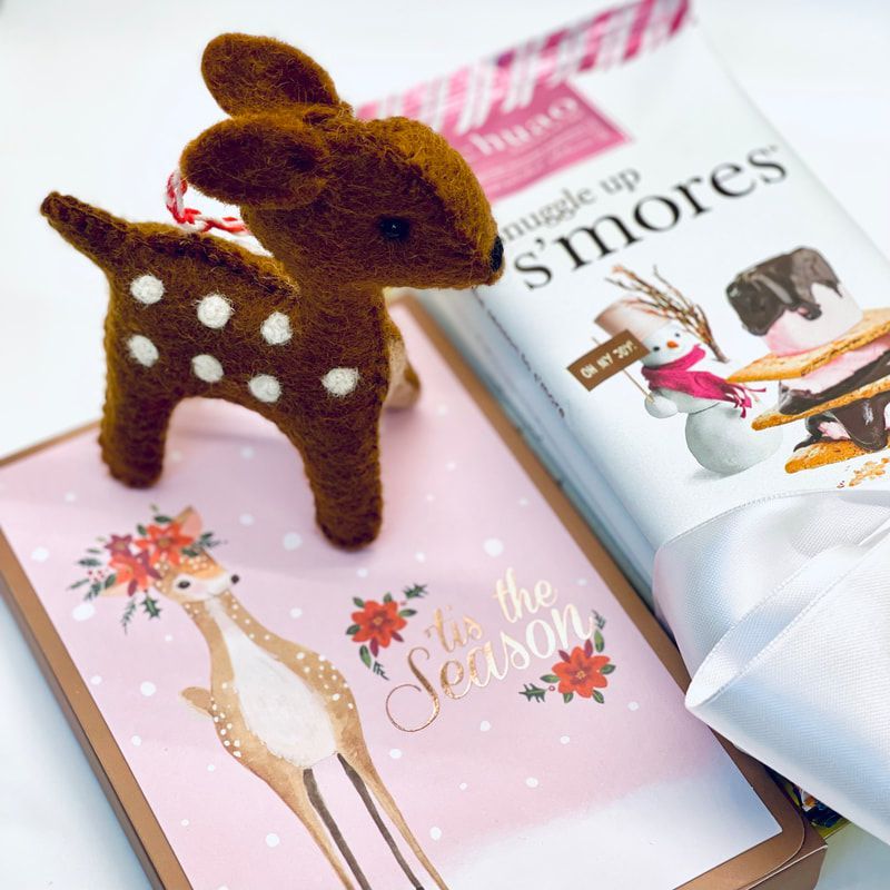 Brown felt fawn figurine beside a pink gift book and ribbon with “s’mores” on the cover