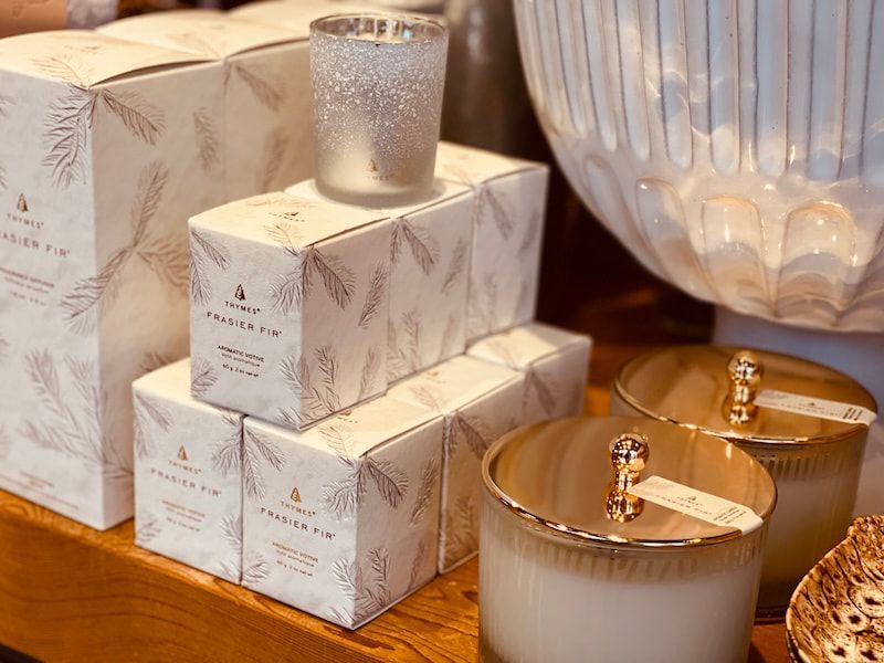 Stacked patterned gift boxes with candles on a wooden surface and a large glass vase in the background