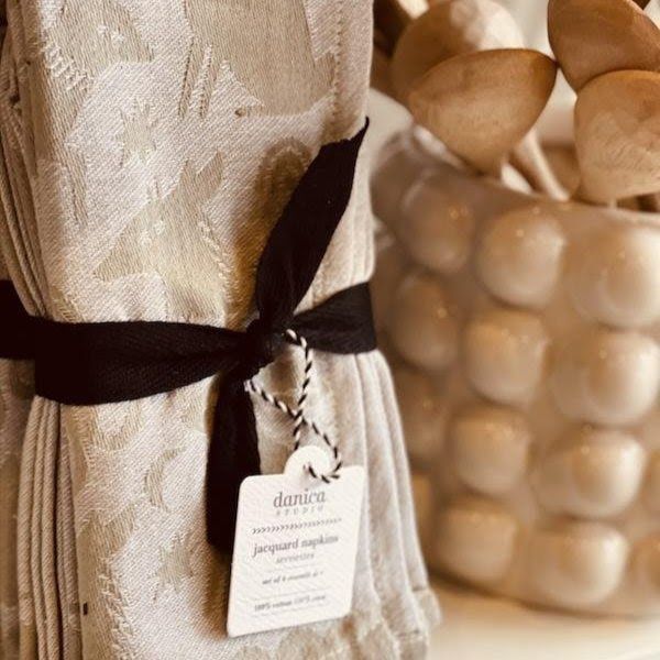 Cream patterned fabric tied with a black ribbon beside a textured glass vase on a wooden surface