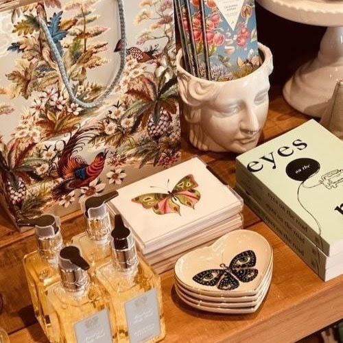Eclectic tabletop display with butterfly decor, glass bottles, a face planter, and stacked eye-themed boxes