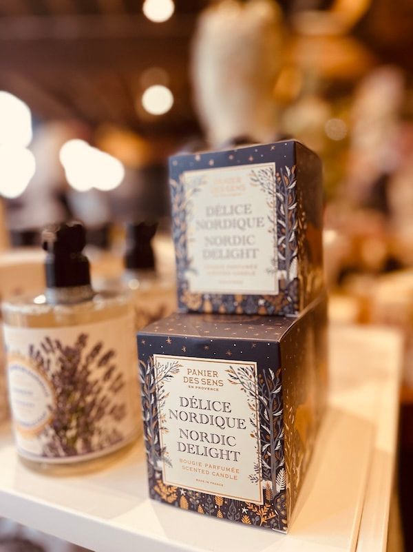 Two perfume bottles and boxes on a shelf, with navy and gold packaging against a blurred warm background