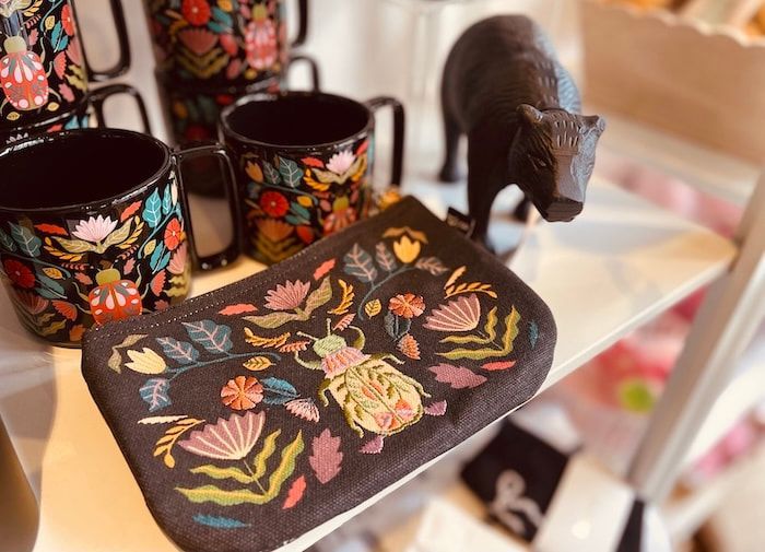 Two black floral mugs and a matching tray with a small black cat figurine on a shelf