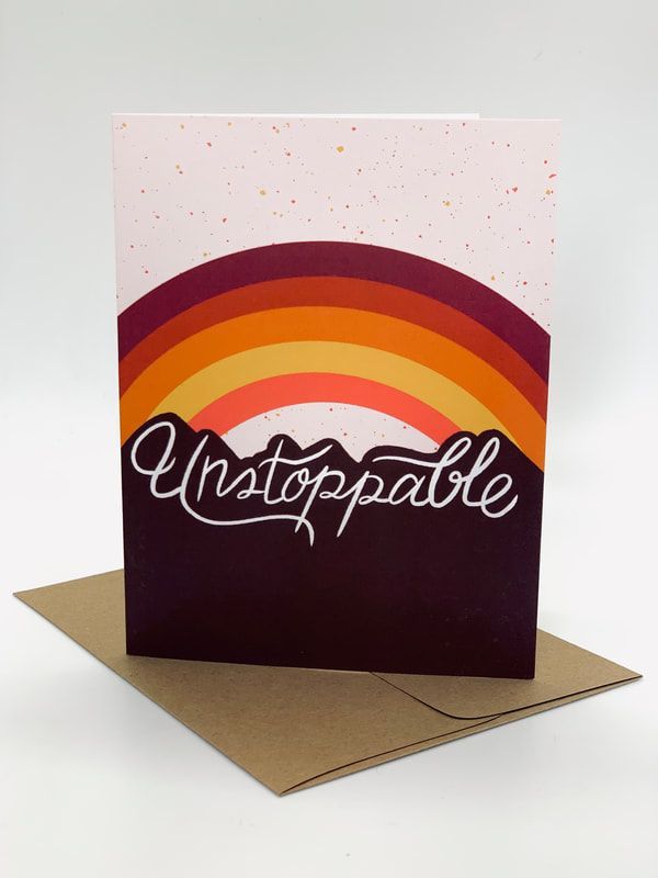 Greeting card with a rainbow arc and the word “Unstoppable” on a folded kraft card stand.