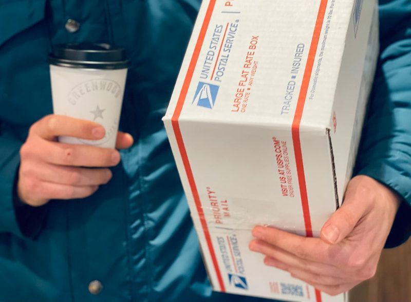 Person in teal jacket holding a coffee cup and a white medical box with red stripe