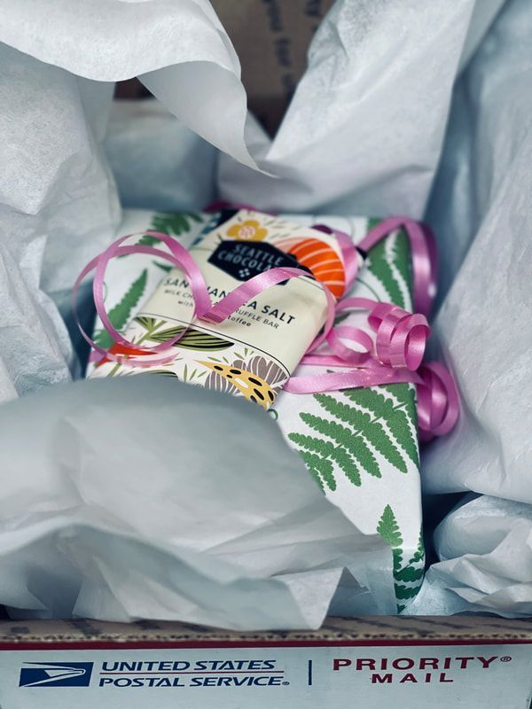Gift box with pastel tissue paper, pink ribbon, and patterned card inside a USPS Priority Mail box