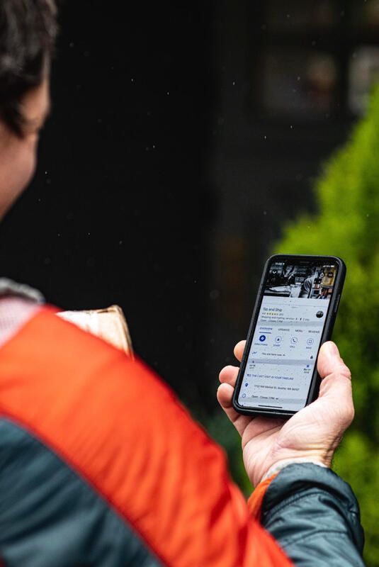 Person in an orange jacket holding a smartphone outdoors and viewing a social media feed