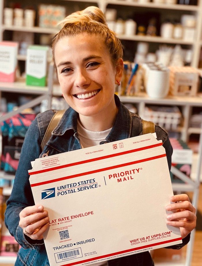 Smiling person holding a USPS Priority Mail box in a postal store