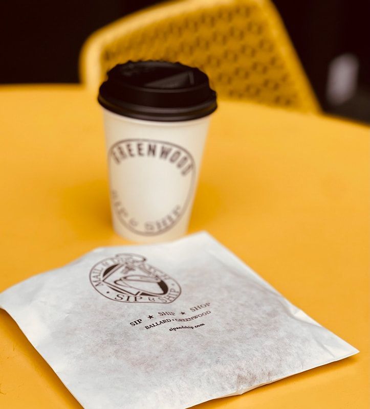 Coffee cup and wrapped pastry on a yellow table, with a blurred chair in the background