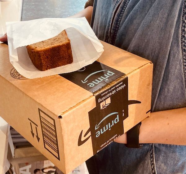 Person holding a cardboard package with a small cake in a paper tray on top