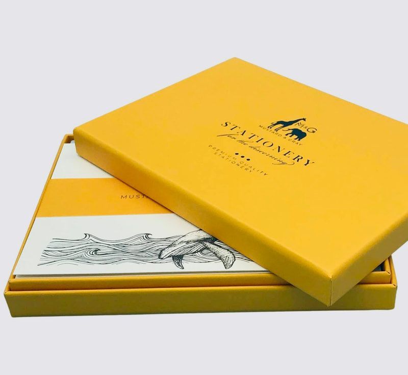 Yellow gift box with a matching lid, showing a black logo and a white sketch insert underneath