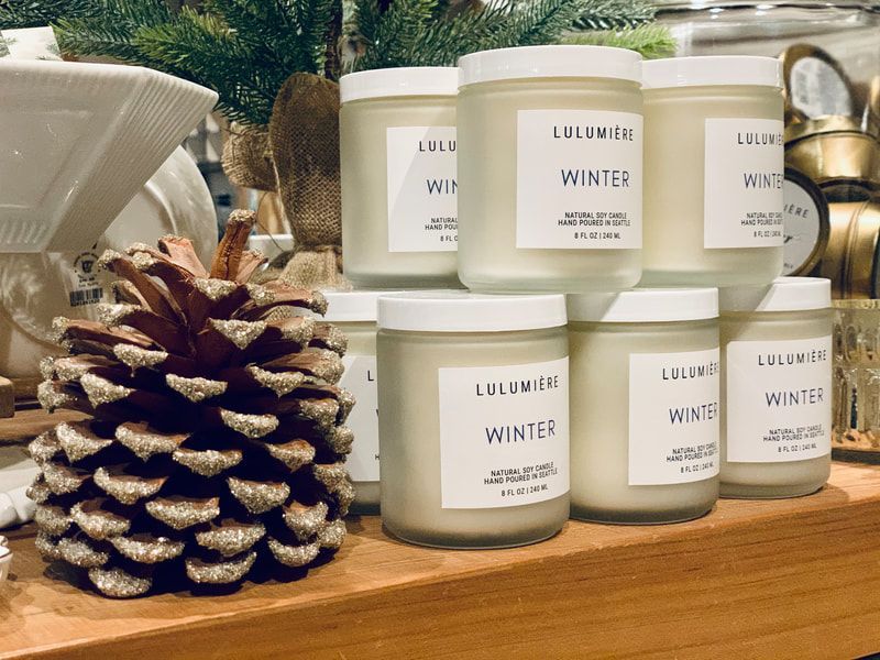 White winter-scented candles and a pinecone on a wooden tray in a cozy holiday display