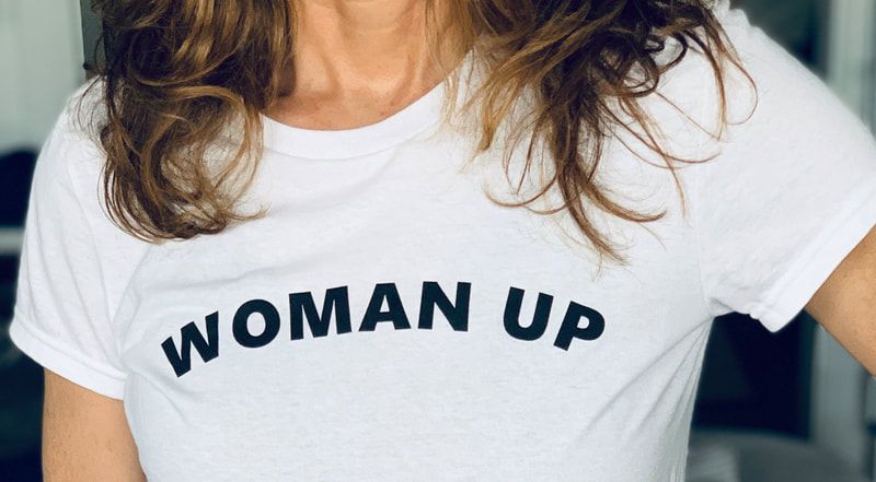 White T-shirt with bold black text “WOMAN UP” across the chest.