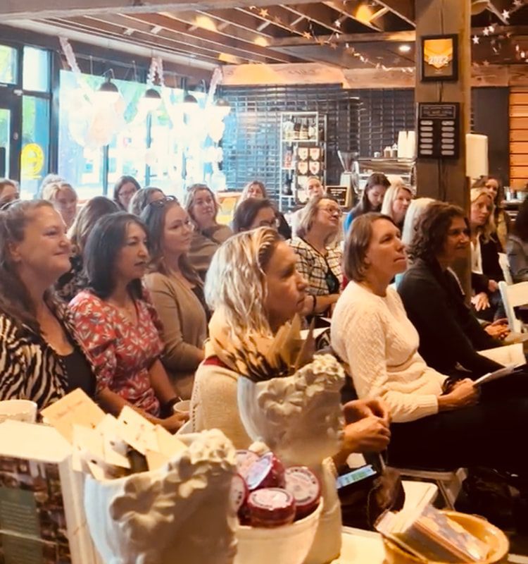 Audience seated indoors at a café-style event, listening attentively under warm lighting.