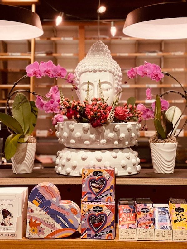 White Buddha statue with pink flowers and red fruit on a decorated shelf in a warm shop display