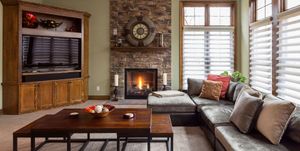 Cozy living room with brick fireplace, sectional sofa, wooden coffee table, and large windows with blinds