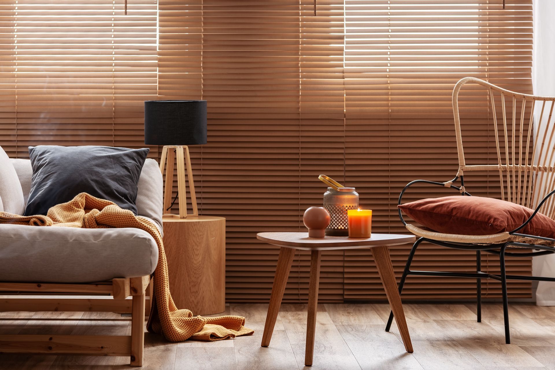 Cozy living room with a chair, side table, lamp, candles, and woven blinds in warm brown tones