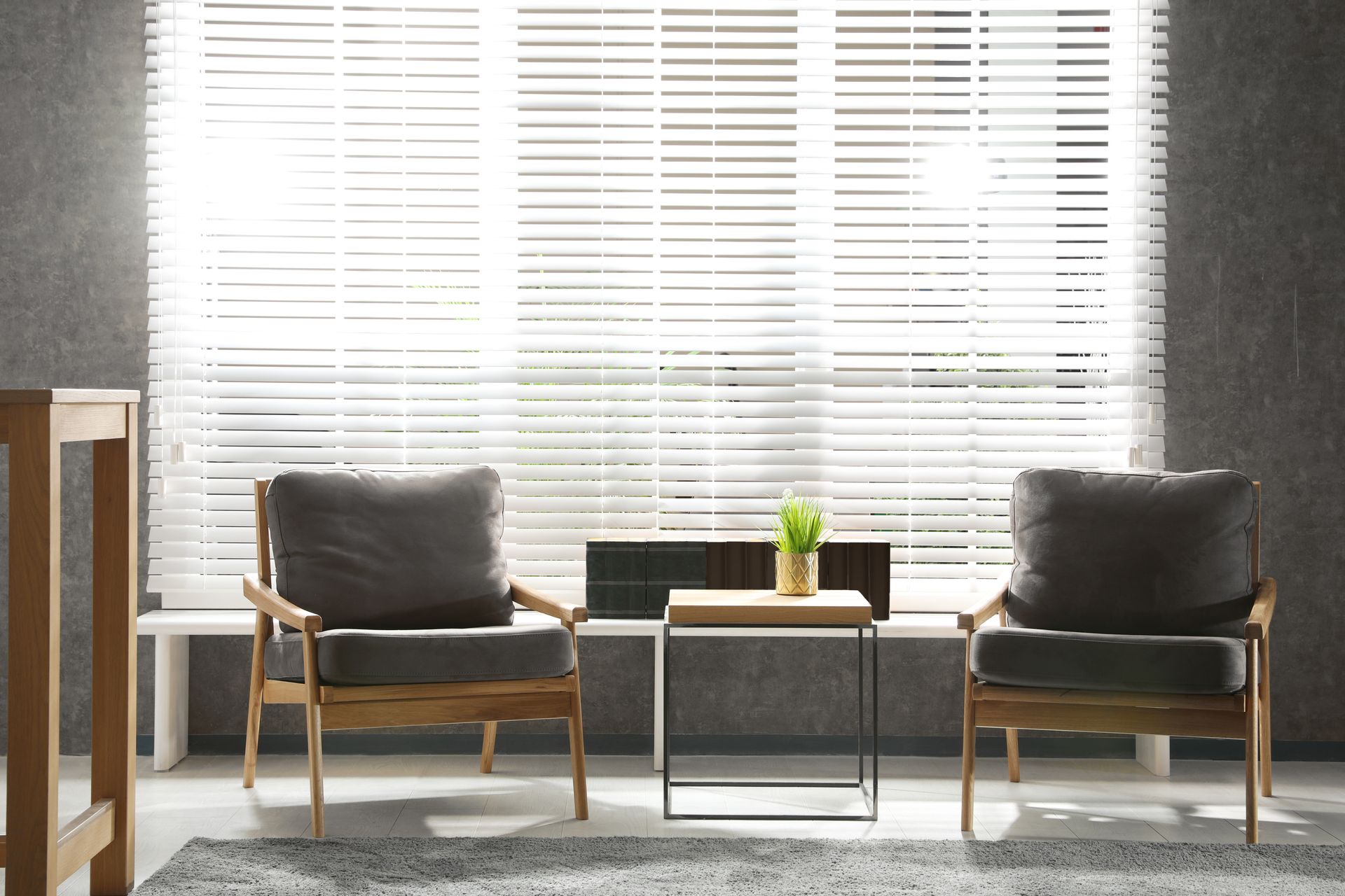 Modern waiting area with two gray armchairs, a small table, and bright blinds in the background Modern waiting area with two gray armchairs, a small table, and bright blinds in the background