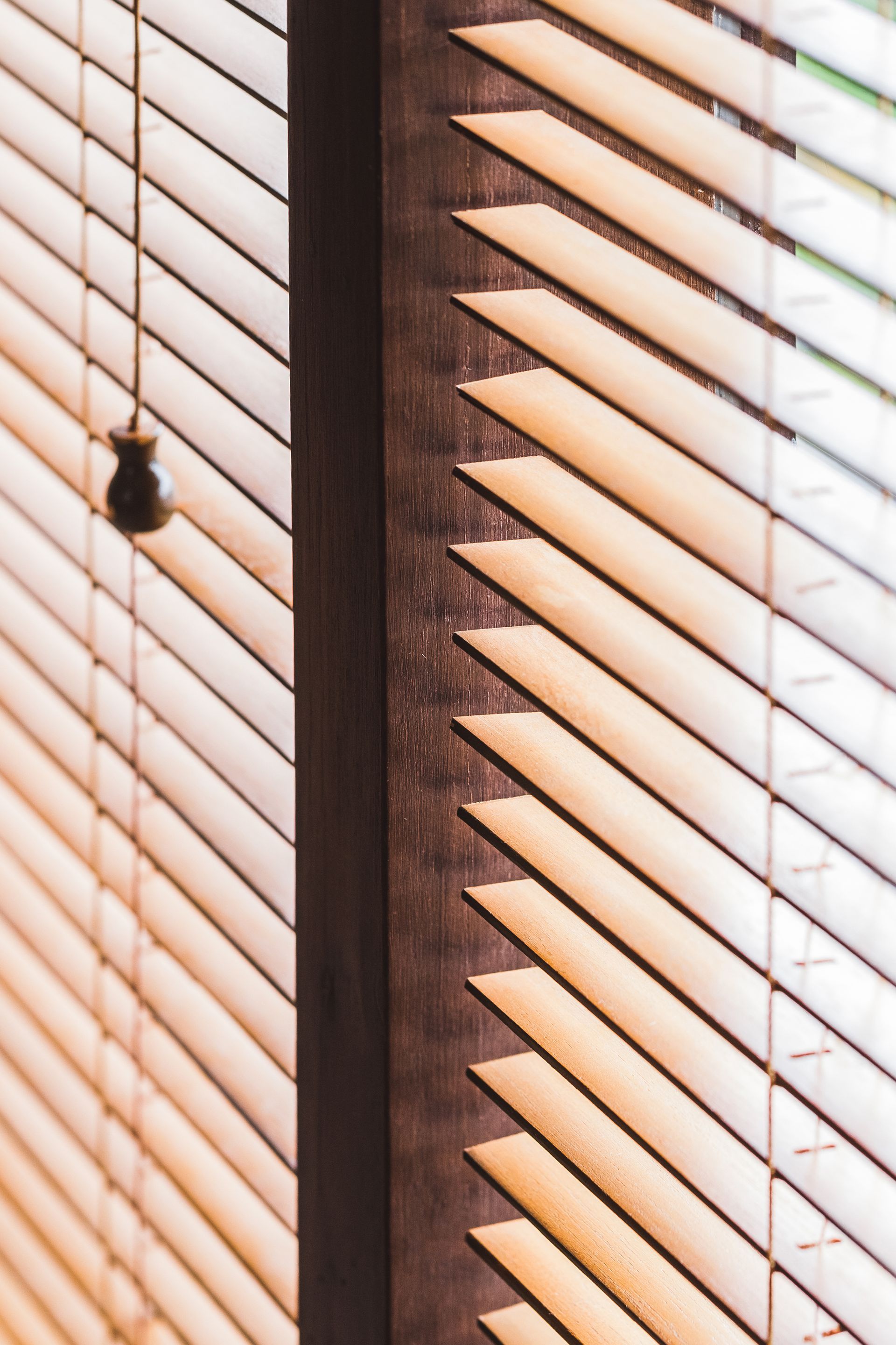 Closed white window blinds with warm sunlight and a hanging pull cord