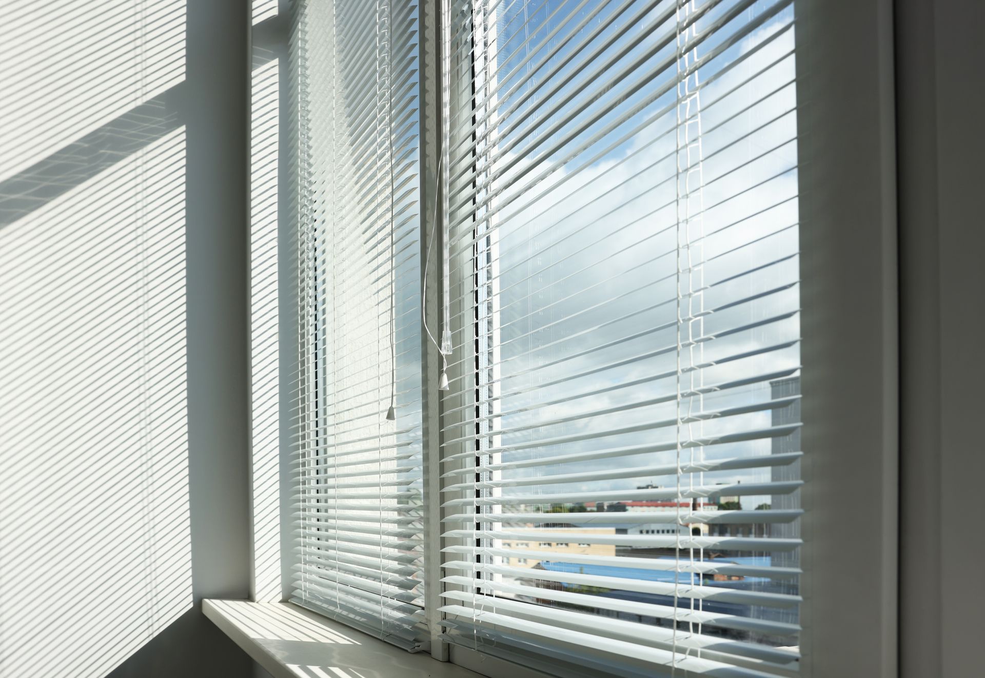 Sunlit office window with white blinds casting shadows on a wall and windowsill