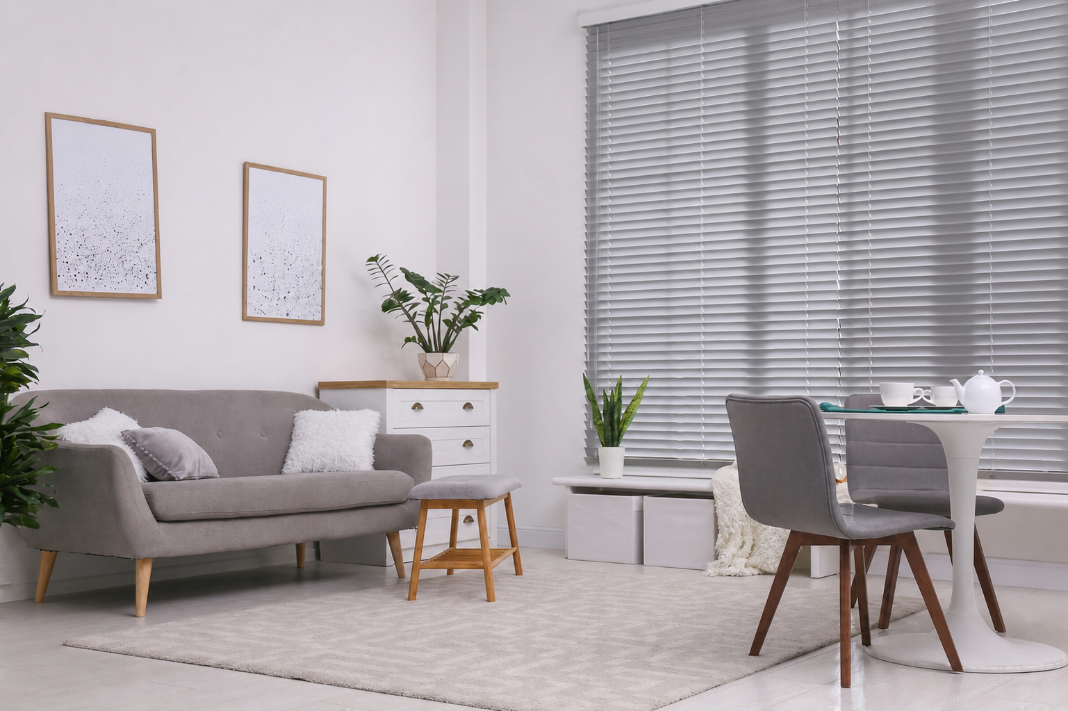 Bright modern living room with gray sofa, dining table, plants, and large window blinds Bright modern living room with gray sofa, dining table, plants, and large window blinds