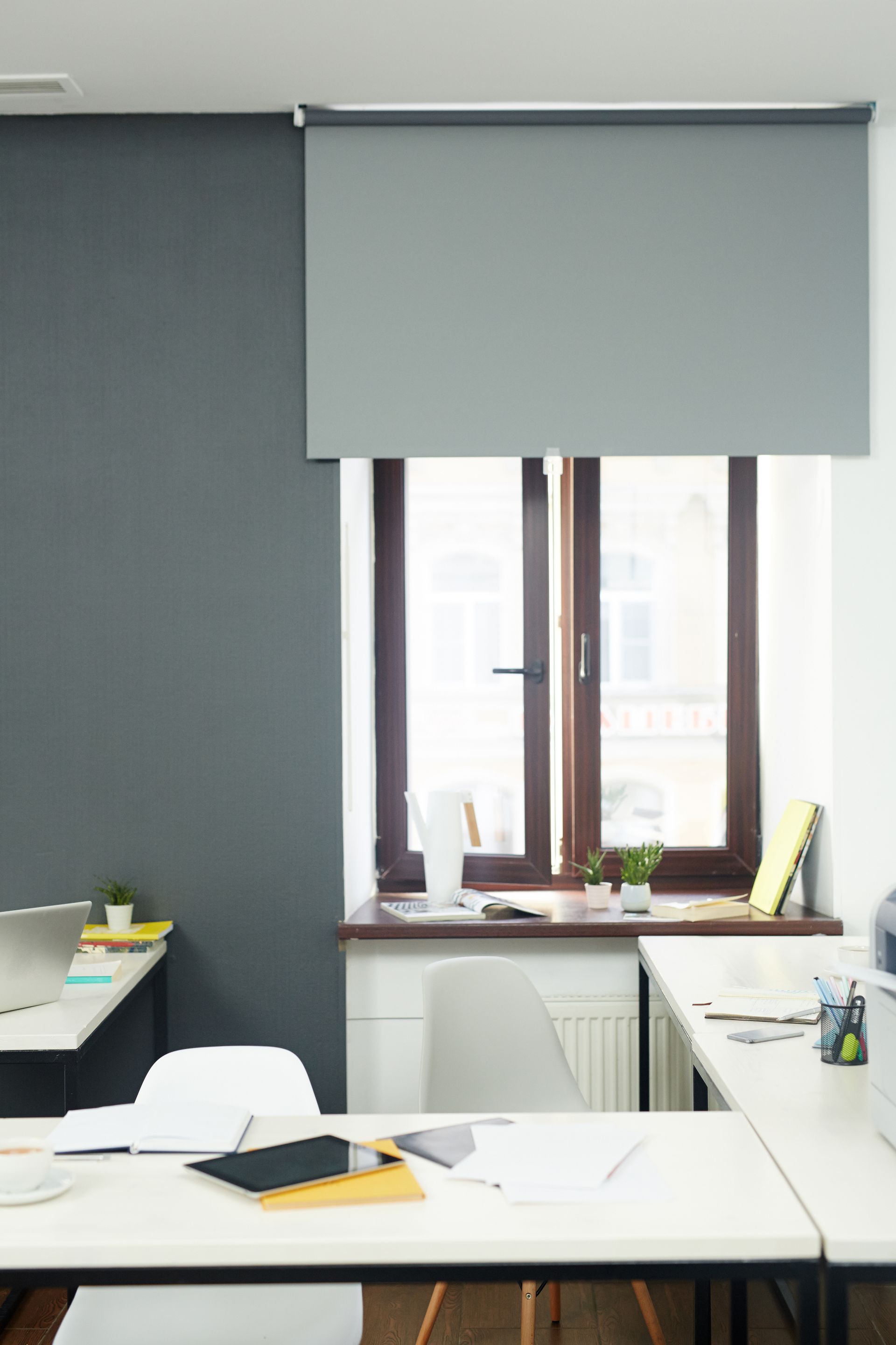 Quiet office with a large window, white desk, and gray roller blind.