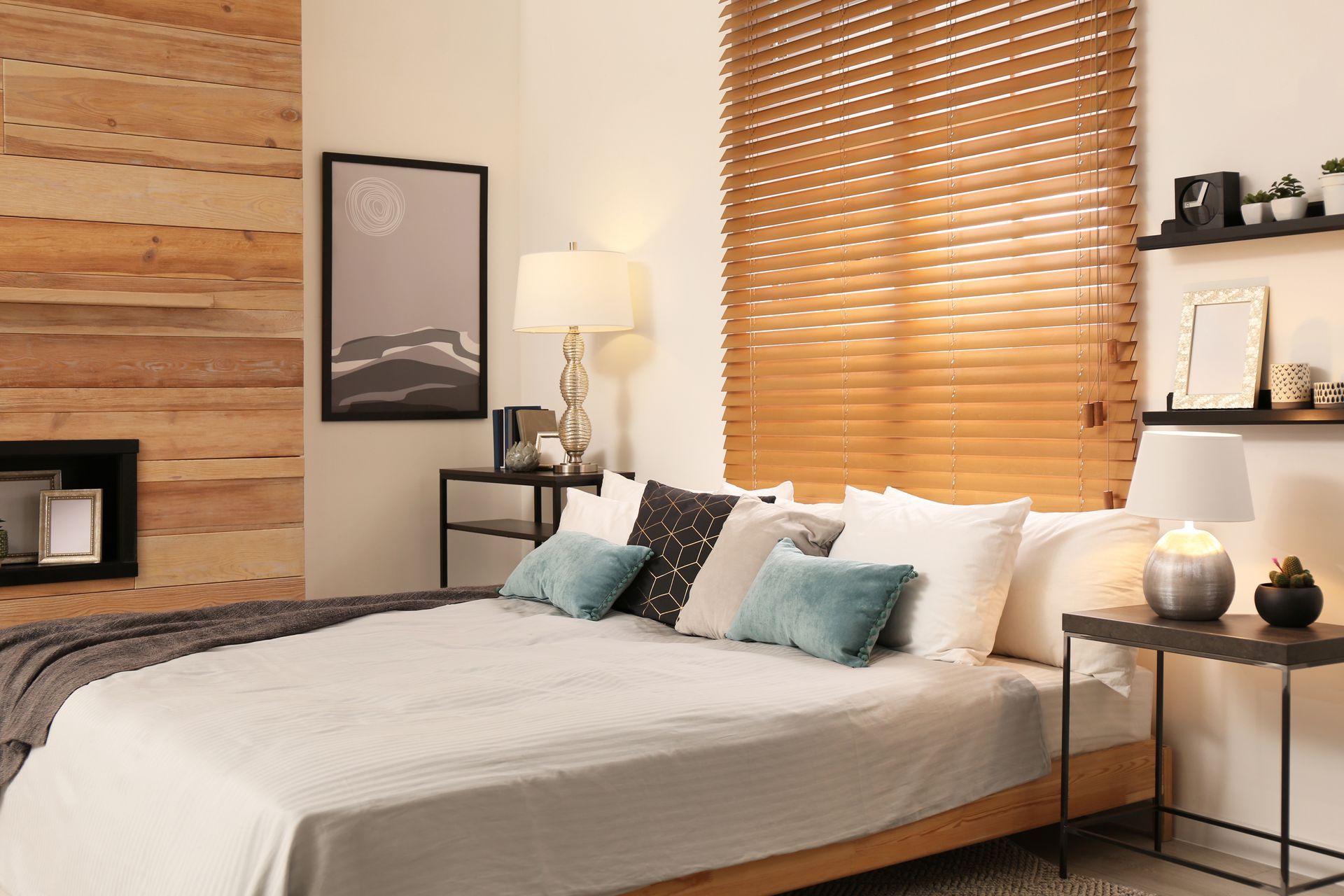 Cozy bedroom with a white bed, teal pillows, wood wall, and woven blinds by a window