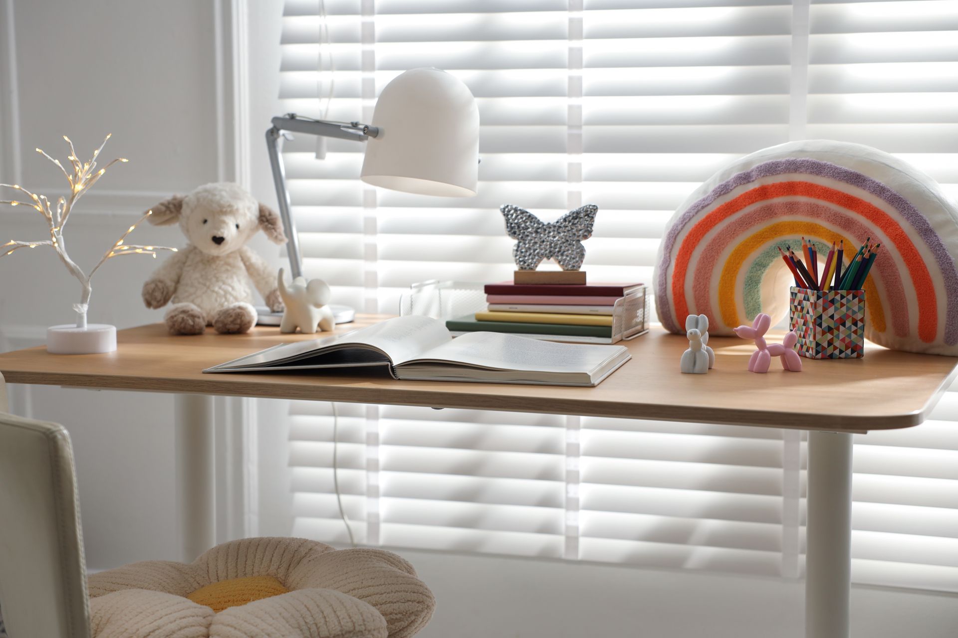 Cozy desk by window with lamp, books, butterfly decor, rainbow art, and stationery on a wooden tabletop Cozy desk by window with lamp, books, butterfly decor, rainbow art, and stationery on a wooden tabletop