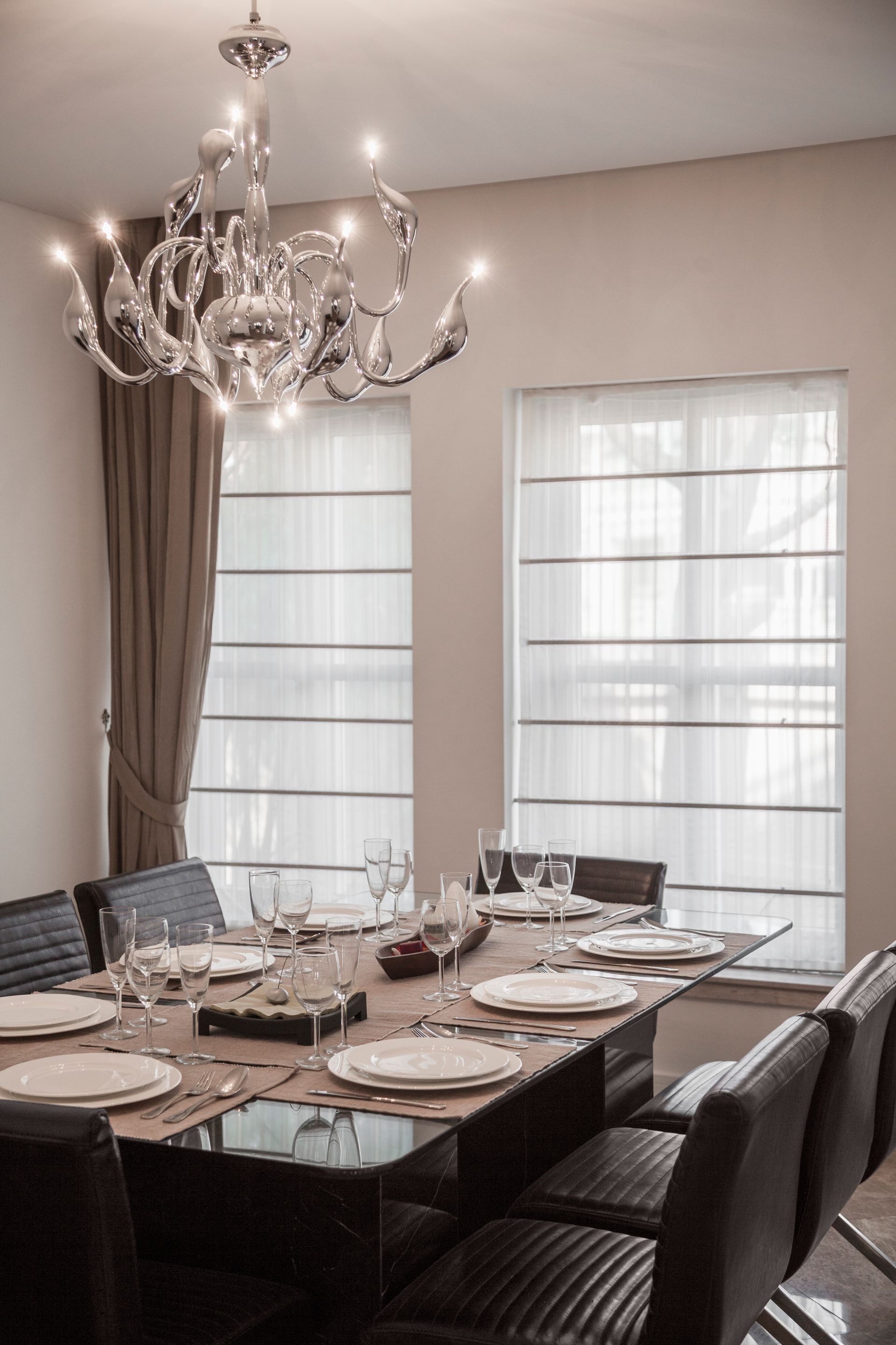Elegant dining room with chandelier, large windows, and a set table around a dark wood table Elegant dining room with chandelier, large windows, and a set table around a dark wood table