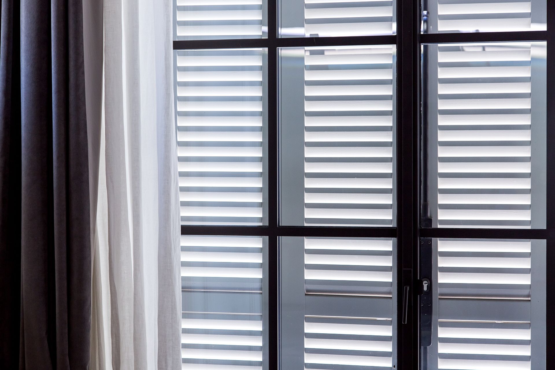 Curtained window with white shutters and black framing, lit by daylight