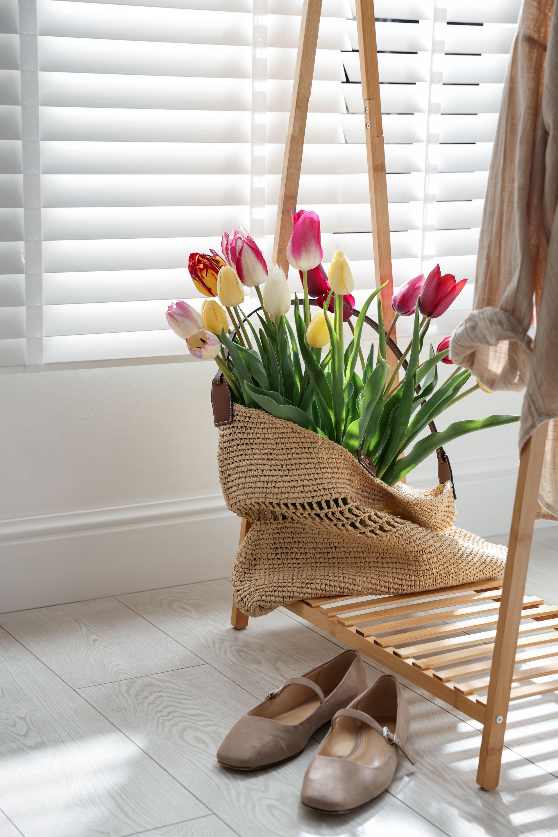 Woven basket of pink and yellow tulips beside a wooden chair and beige shoes by a sunlit window Woven basket of pink and yellow tulips beside a wooden chair and beige shoes by a sunlit window